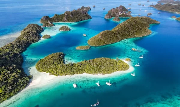 Yachts anchored off a remote white sandy beach in Indonesia.